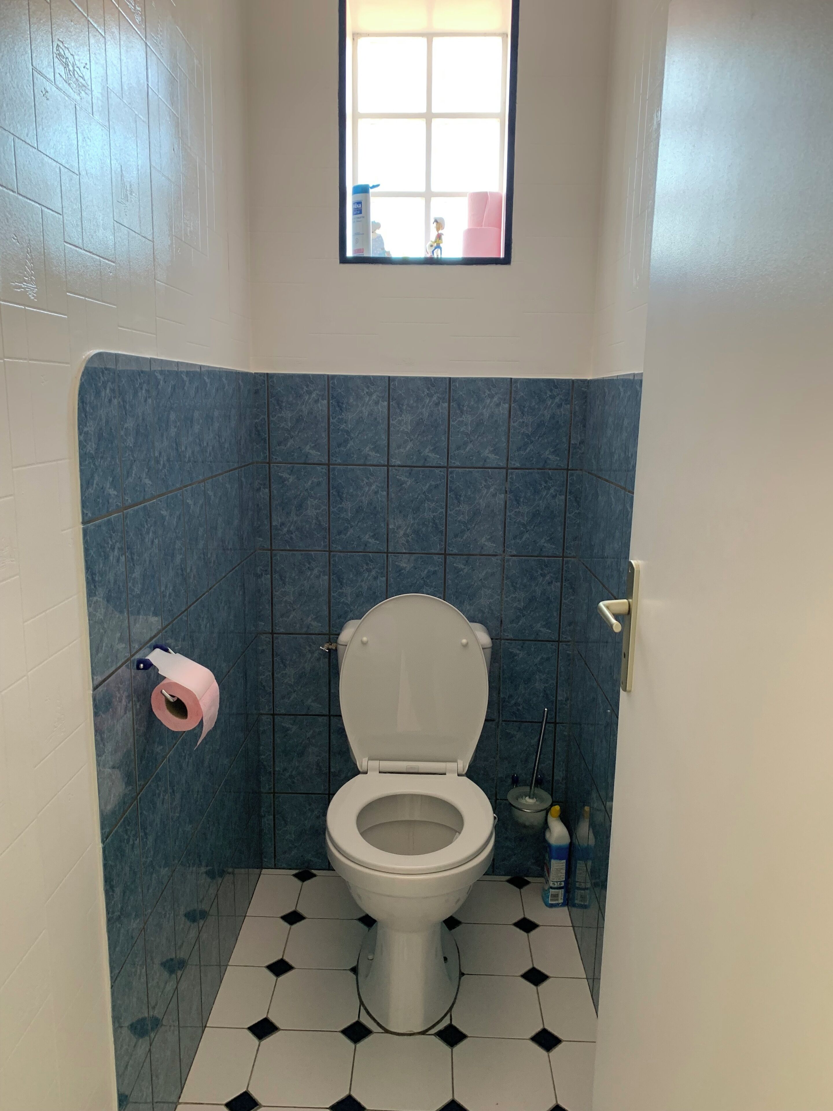 Un bagno con il water, piastrelle blu, una piccola finestra e un portasciugamani.