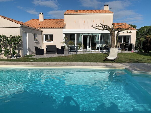 Ein modernes Haus mit Swimmingpool, Sitzgelegenheiten im Freien und einem gepflegten Rasen.