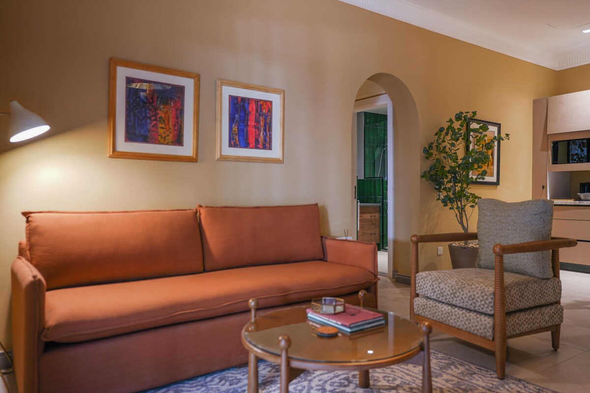 A living room with a sofa, armchair, coffee table, and two framed artworks on the wall.