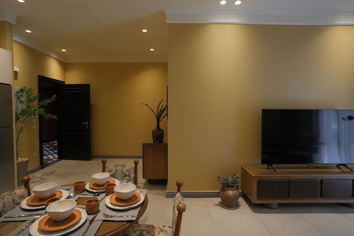 A dining area with a table set for six, a television, and a potted plant.