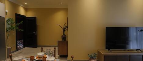 A dining area with a table set for six, a television, and a potted plant.