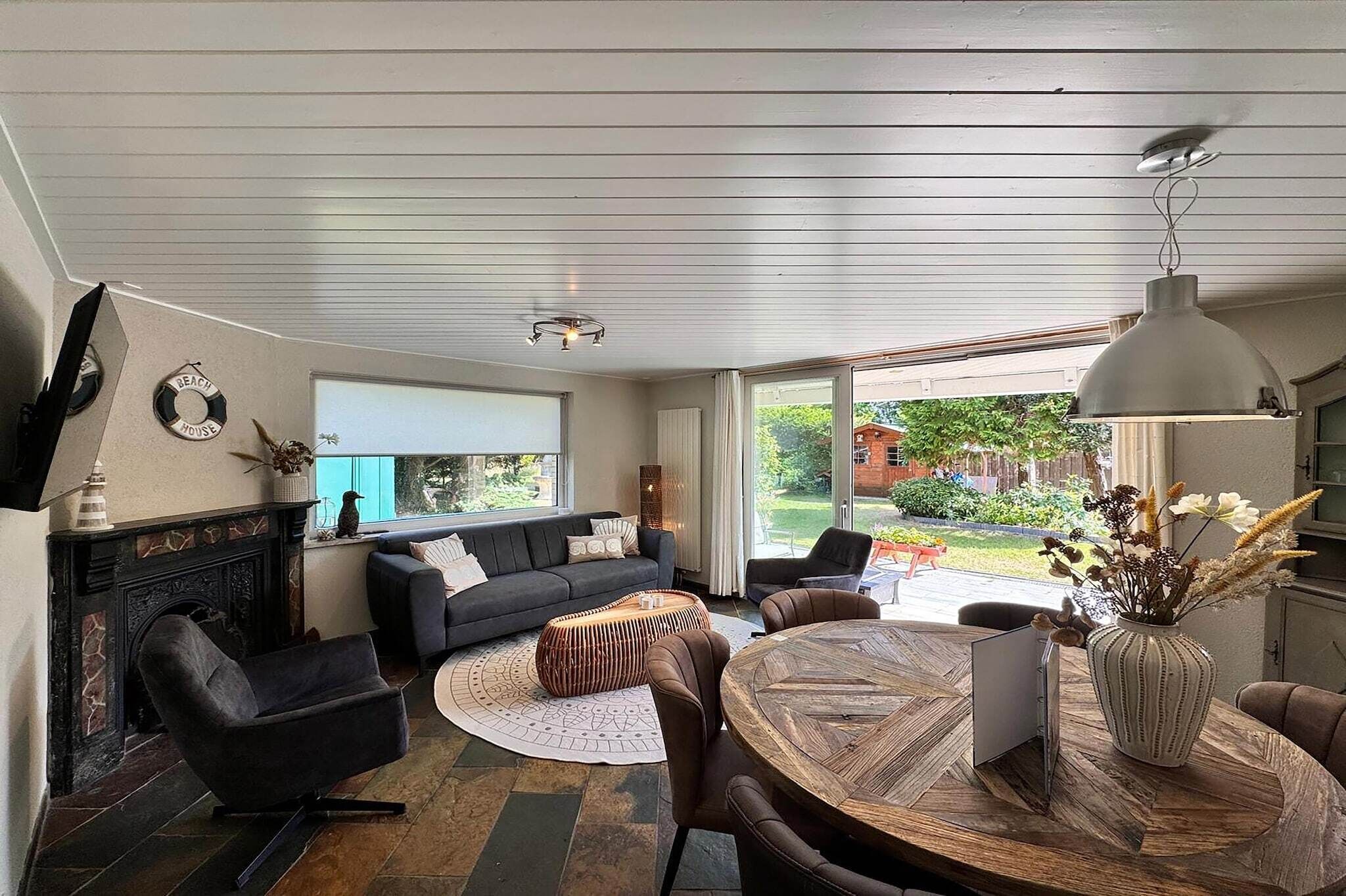 Een moderne woonkamer met een open haard, een bank, een eettafel en een groot raam met uitzicht op de omgeving.