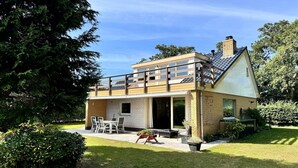Ein zweistöckiges Haus mit Balkon, einer Terrasse mit Gartenmöbeln und einem gepflegten Garten.