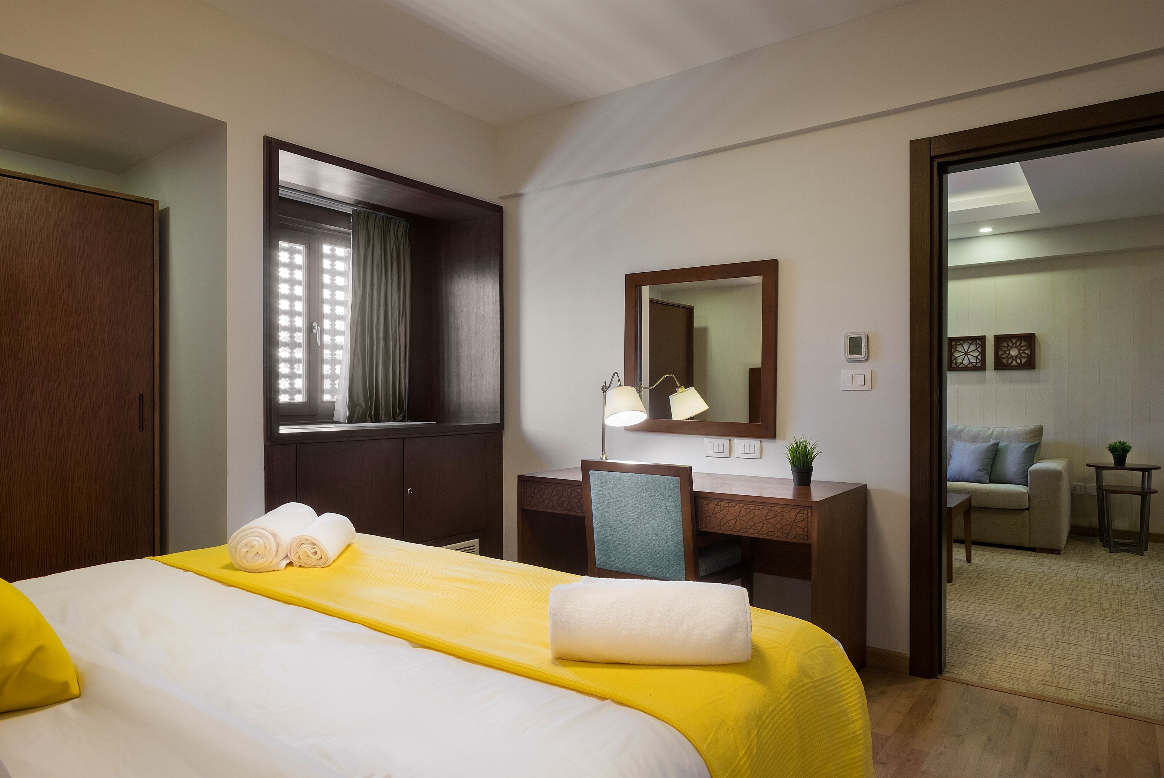 A hotel room with a bed, desk, chair, and a view of the living area.