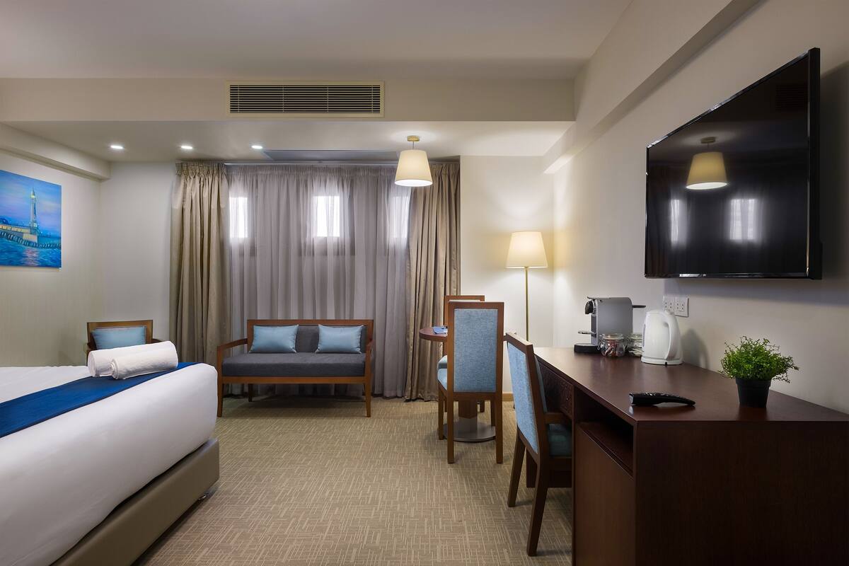 A hotel room with a bed, a sofa, a desk, a chair, a television, and a window with curtains.