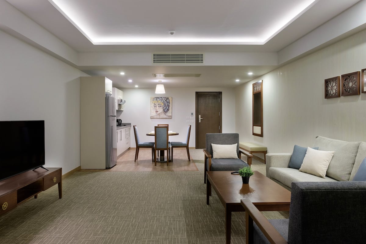 A modern living room with a flat-screen TV, a sofa, a coffee table, and a dining area with chairs and a table.
