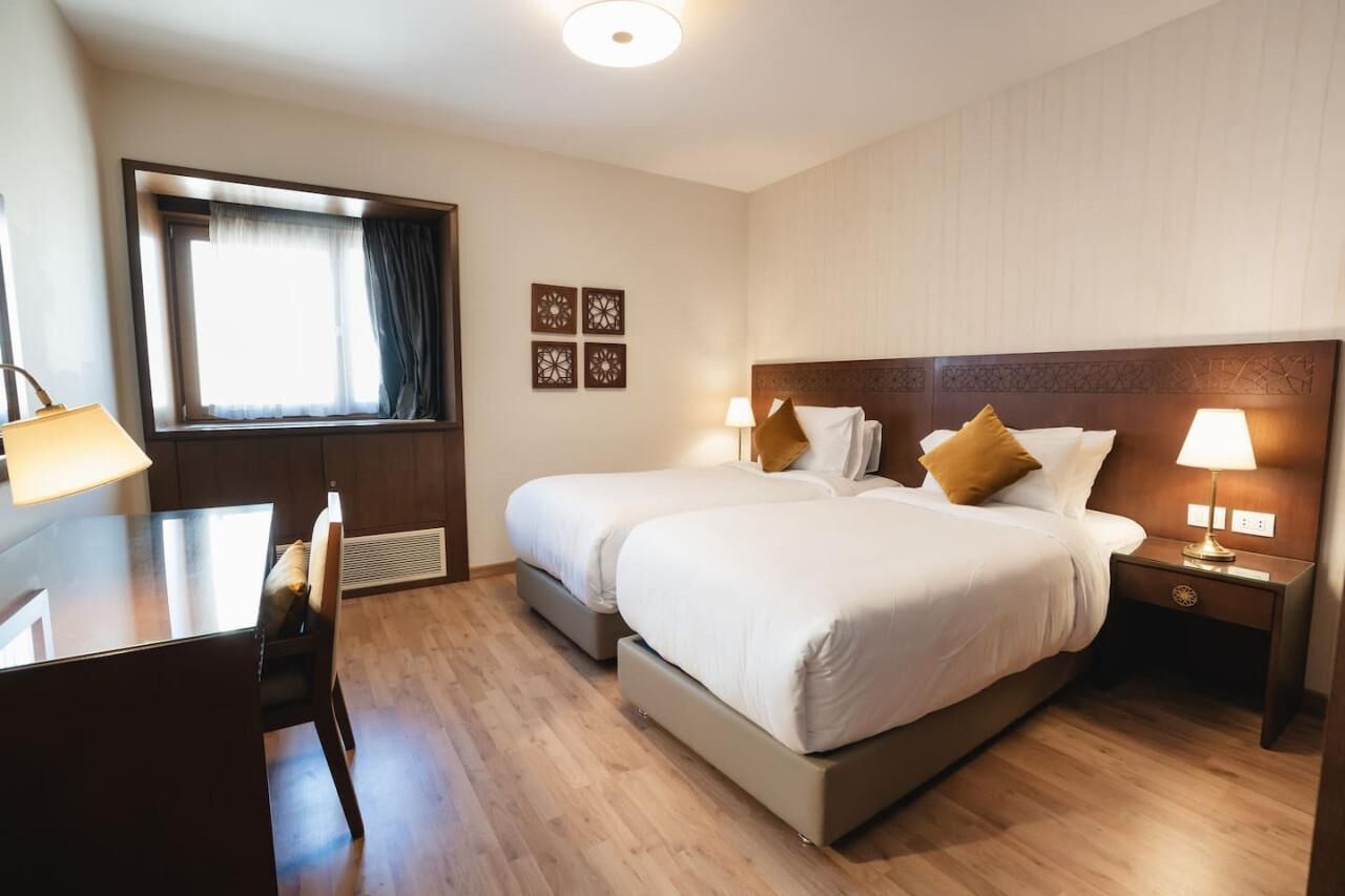 A hotel room with two beds, a desk, and a window with curtains.