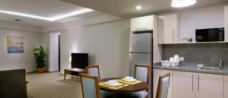 A modern kitchen with a built-in microwave, refrigerator, and sink. There is a dining area with a table and chairs, and a television in the corner.