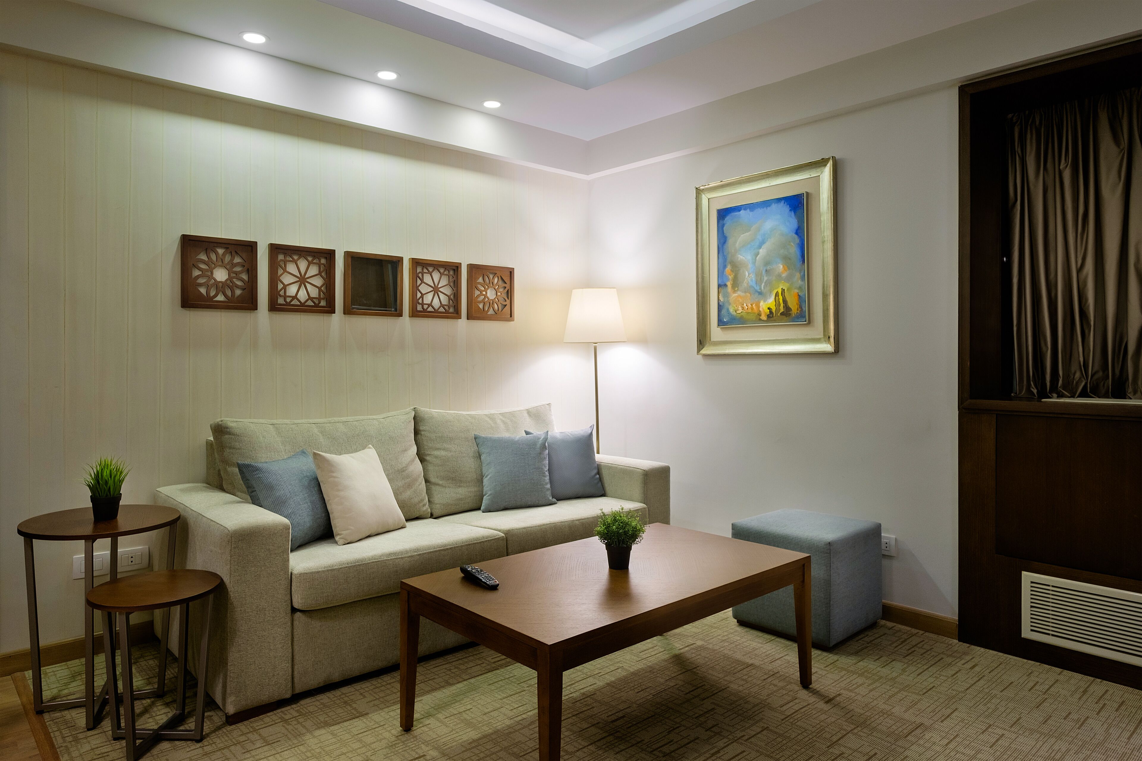 A living room with a sofa, two side tables, a coffee table, a lamp, and a painting on the wall.