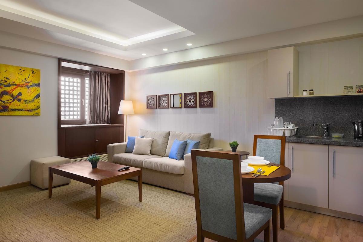 A modern living room with a sofa, coffee table, and dining table. There is a kitchen area with a sink and cabinets.