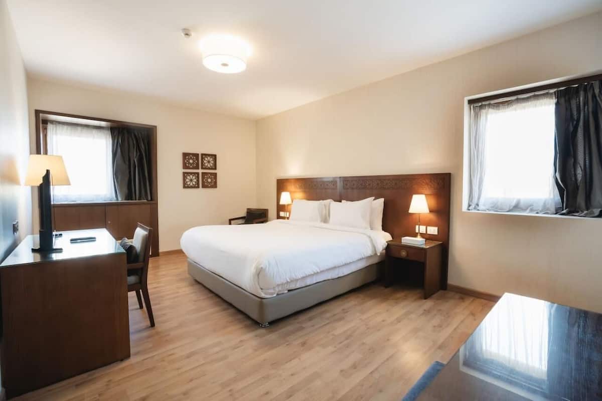 A hotel room with a bed, bedside tables, a desk, and a chair.