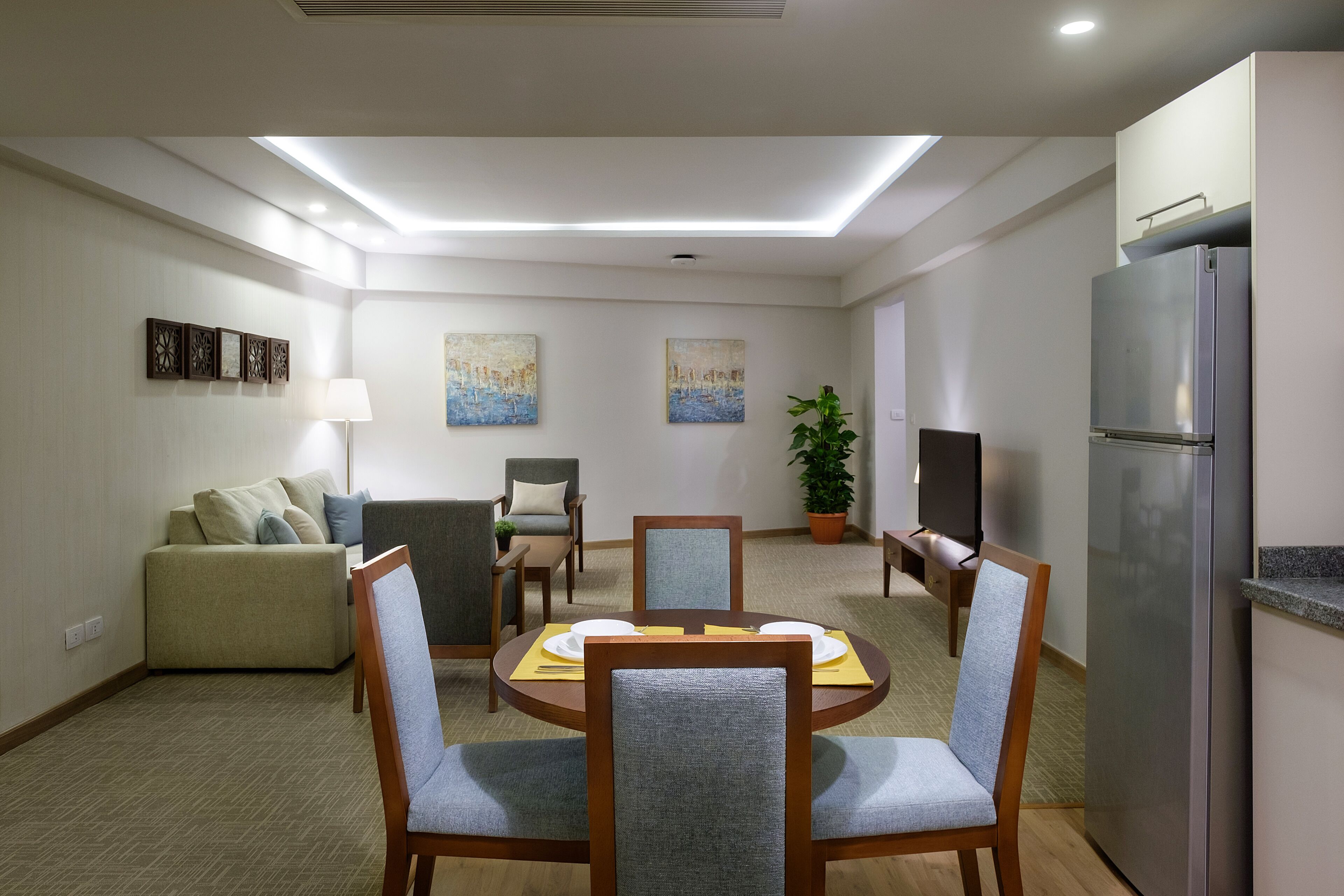 A dining area with a round table, four chairs, a sofa, a TV, and a refrigerator.