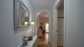 A hallway with a white console table, a mirror, and a lamp. There is a door leading to a room with a bed and a window. - Playa Grande 118 - Two Bedroom Apartment, Sleeps 5 (Punta del moral)