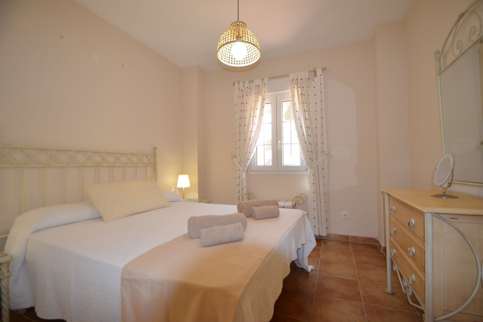 Ein Schlafzimmer mit einem Bett, einem Nachttisch, einer Kommode, einem Spiegel und einem Fenster mit Vorhängen.
