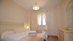 A bedroom with a bed, a bedside table, a dresser, a mirror, and a window with curtains. - Playa Grande 118 - Two Bedroom Apartment, Sleeps 5 (Punta del moral)