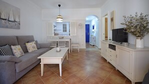 A living room with a sofa, coffee table, and TV stand. There is a kitchen area with a sink and a dining table. - Playa Grande 118 - Two Bedroom Apartment, Sleeps 5 (Punta del moral)