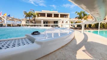 Uma área de piscina com espreguiçadeira, cadeira de piscina e um edifício com várias varandas ao fundo.