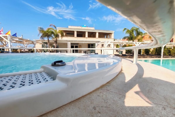 A pool area with a lounge chair, a poolside chair, and a building with multiple balconies in the background. - Pino Residence (Nardò)