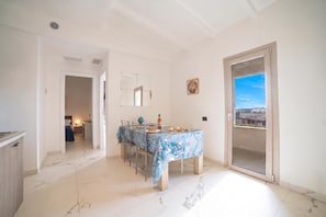 A dining area with a table set for two, a sliding glass door to a balcony, and a view of the cityscape. - Pino Residence (Nardò)