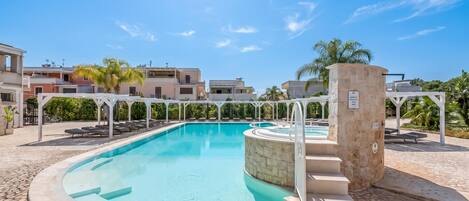 A swimming pool with a stone border, a stone pillar, and a pergola structure.