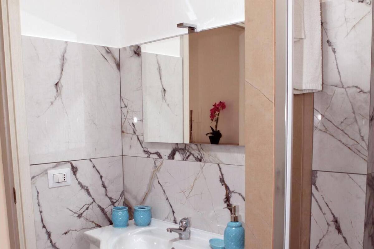 A bathroom with a white sink, marble walls, and a blue rug.