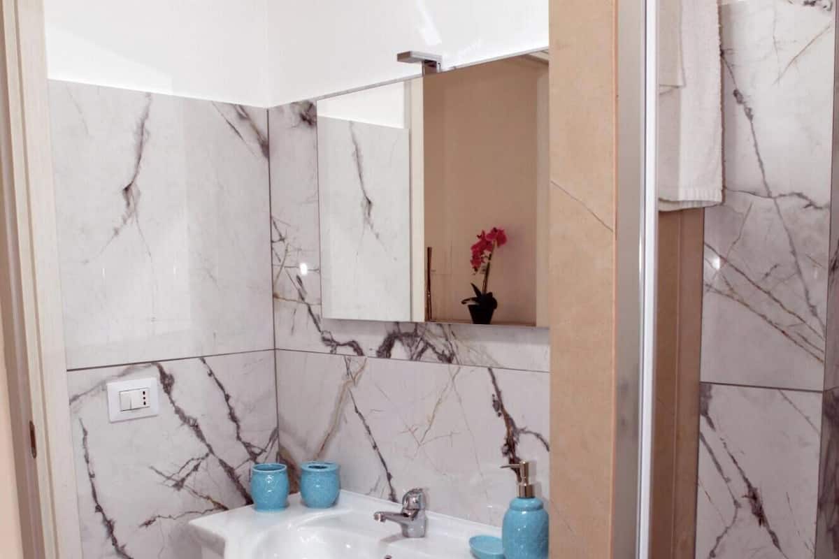 A bathroom with a marble backsplash, a white sink, and a mirror above it. There are two blue soap dispensers on the sink.