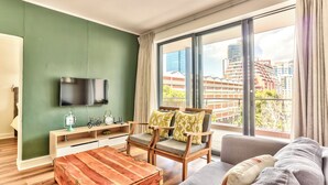 Un salón moderno con un ventanal grande, un televisor de pantalla plana, una mesa de centro de madera y un sofá.