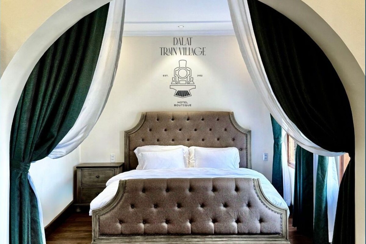A bedroom with a tufted headboard bed, a nightstand, and a wall-mounted sign indicating the establishment year and name.