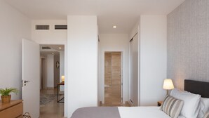 Une chambre d’hôtel moderne avec un grand lit, une table de chevet, une lampe et une vue sur un couloir.