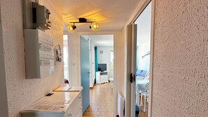A hallway with a kitchen area, a dining table, and a TV in the background. - Sun, peace & comfort in Port Camargue (Le Grau-du-Roi)