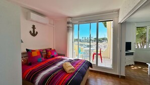 A bedroom with a bed, colorful pillows, a view of a marina, and a balcony with chairs. - Sun, peace & comfort in Port Camargue (Le Grau-du-Roi)