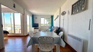 A spacious living area with a dining table, white chairs, a sofa, and a television. - Sun, peace & comfort in Port Camargue (Le Grau-du-Roi)
