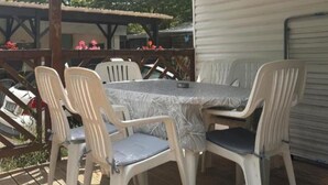 Een overdekt terras met een tafel en stoelen, een houten terras en een gebouw met een garage.