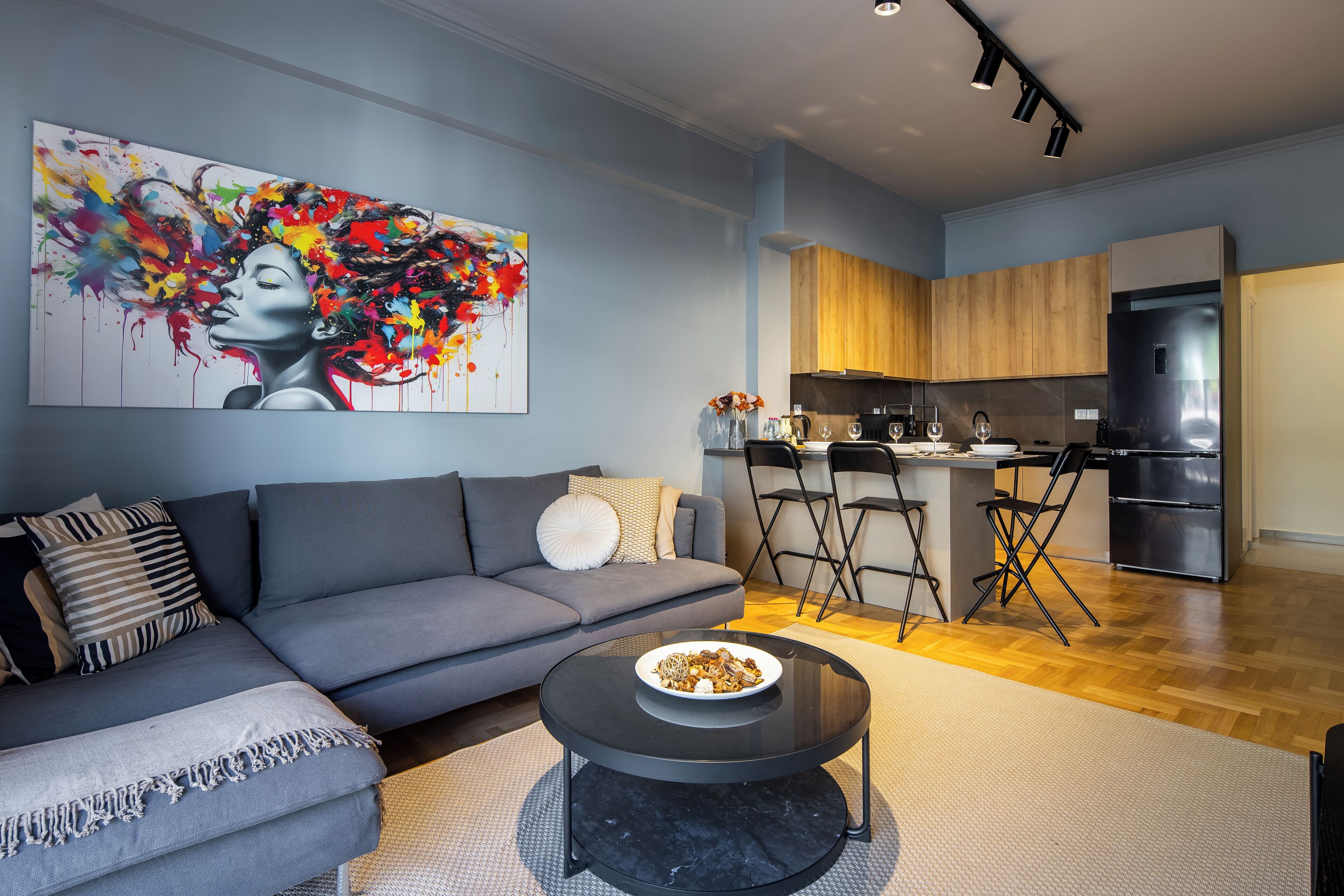 Un soggiorno moderno con un divano grigio, un tavolino da caffè nero e un quadro astratto colorato appeso al muro.