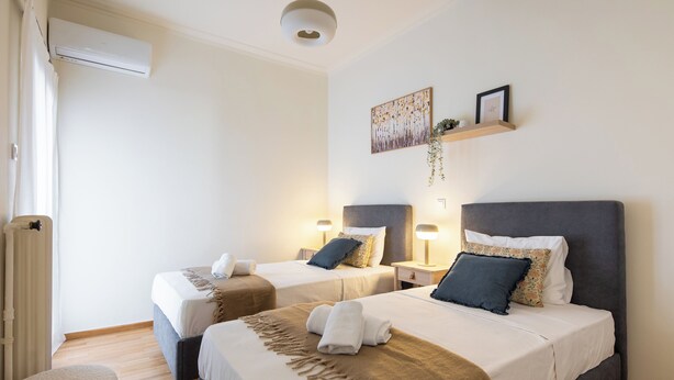A hotel room with two beds, a small seating area, and a wall-mounted shelf with decorative items. - Zephyr 3-Bedroom Apartment in Athens (Athens)