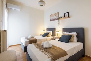 Une chambre d’hôtel avec deux lits, un petit coin salon et une étagère fixée au mur, ornée d’objets décoratifs.