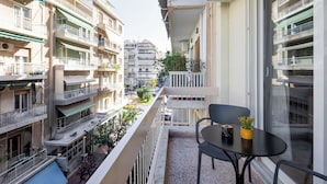 A balcony with a table and chairs, overlooking a street with buildings. - Zephyr 3-Bedroom Apartment in Athens (Athens)