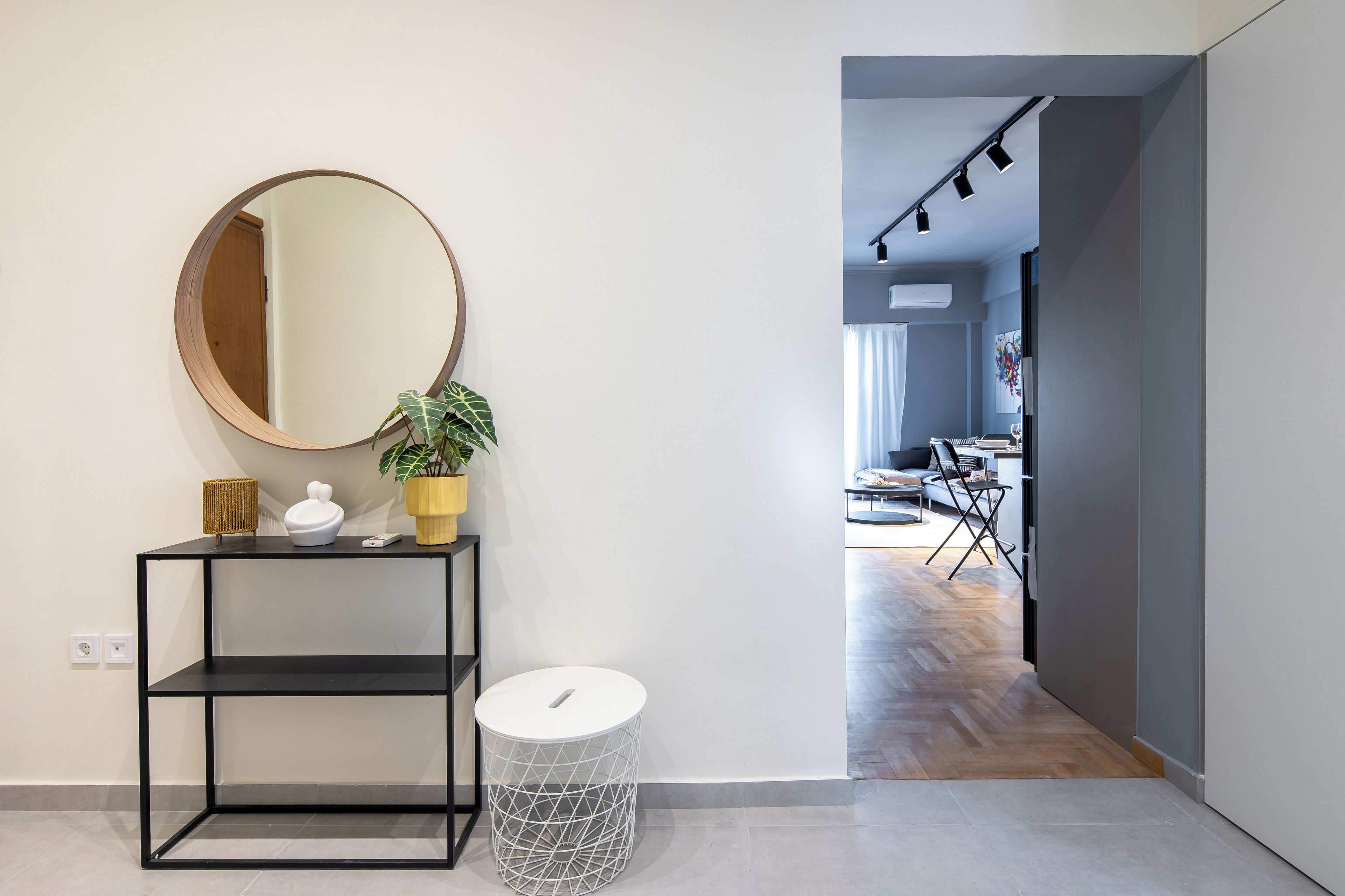 A modern interior with a round mirror, a potted plant, a white trash bin, and a black console table.