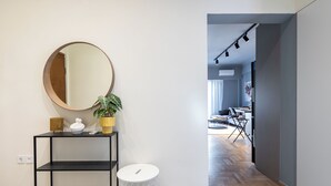 A modern interior with a round mirror, a potted plant, a white trash bin, and a black console table. - Zephyr 3-Bedroom Apartment in Athens (Athens)