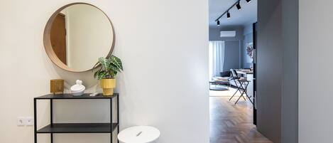 A modern interior with a round mirror, a potted plant, a white trash bin, and a black console table.