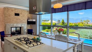 A modern kitchen with a gas stove, a brick wall, and a large window overlooking a garden. - Villa Limon (Kusadasi)