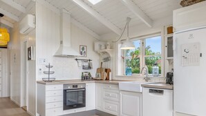 Une cuisine moderne avec des meubles blancs, un four encastré et une fenêtre donnant sur un paysage verdoyant.