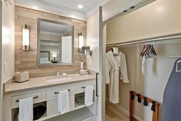 Un baño moderno con tocador de madera, un espejo grande y un vestidor con bata y ropa colgada.