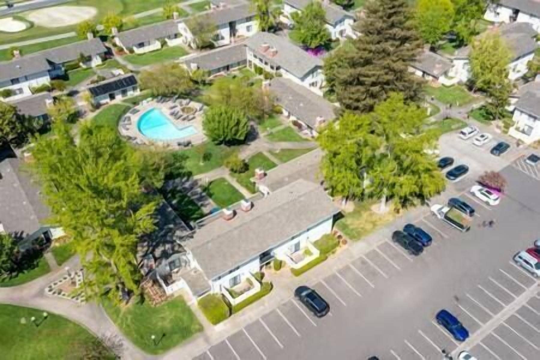 An aerial view of a residential area with houses, a swimming pool, and a parking lot.