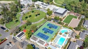 Eine Vogelperspektive zeigt eine Wohngegend mit einem großen Tennisplatz, einem Schwimmbad und mehreren Häusern.