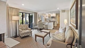 Ein großzügiges Wohnzimmer mit einer Couch, einem Sessel und einem Couchtisch, ein Essbereich mit Tisch und Stühlen sowie eine Küche mit modernen Geräten.