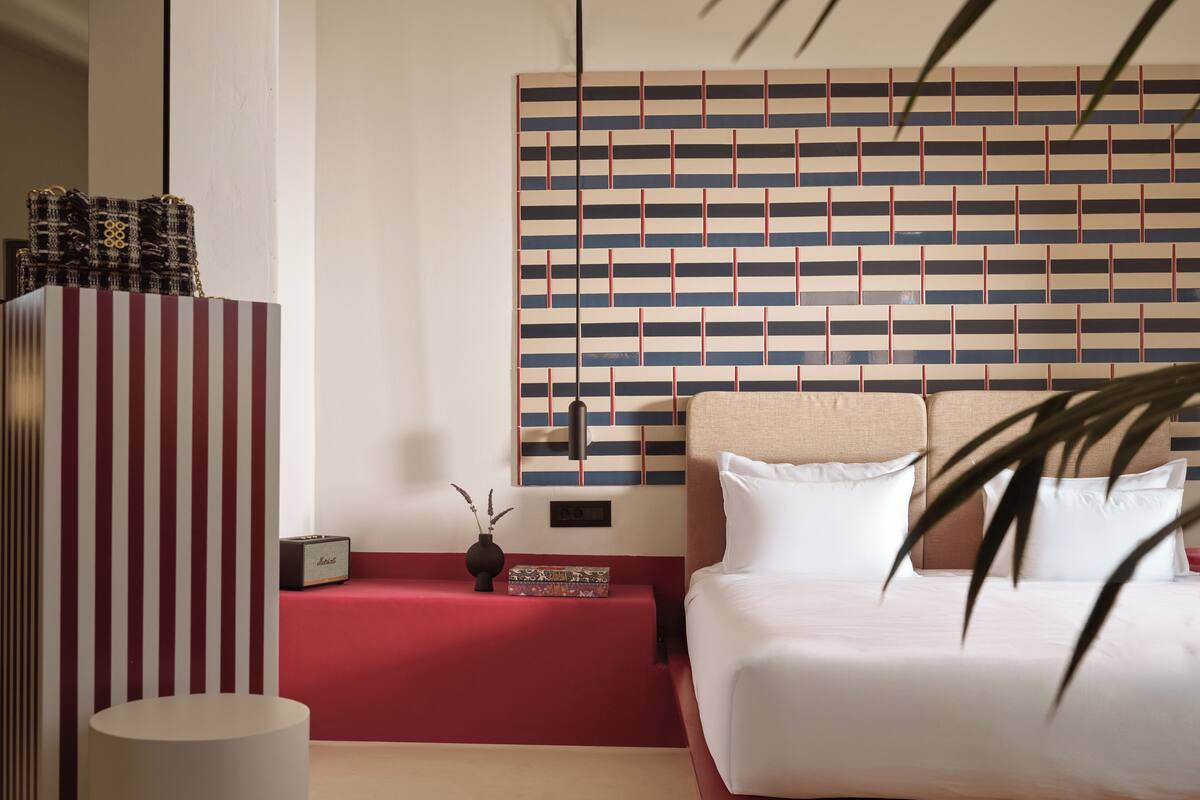 Een moderne hotelkamer met een groot bed, een rode accentmuur, een gestreept hoofdeinde en een klein nachtkastje met een vaas.