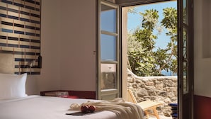 Ein Hotelzimmer mit Bett, Nachttisch, Lampe, Fenster und Blick auf Meer und Bäume.