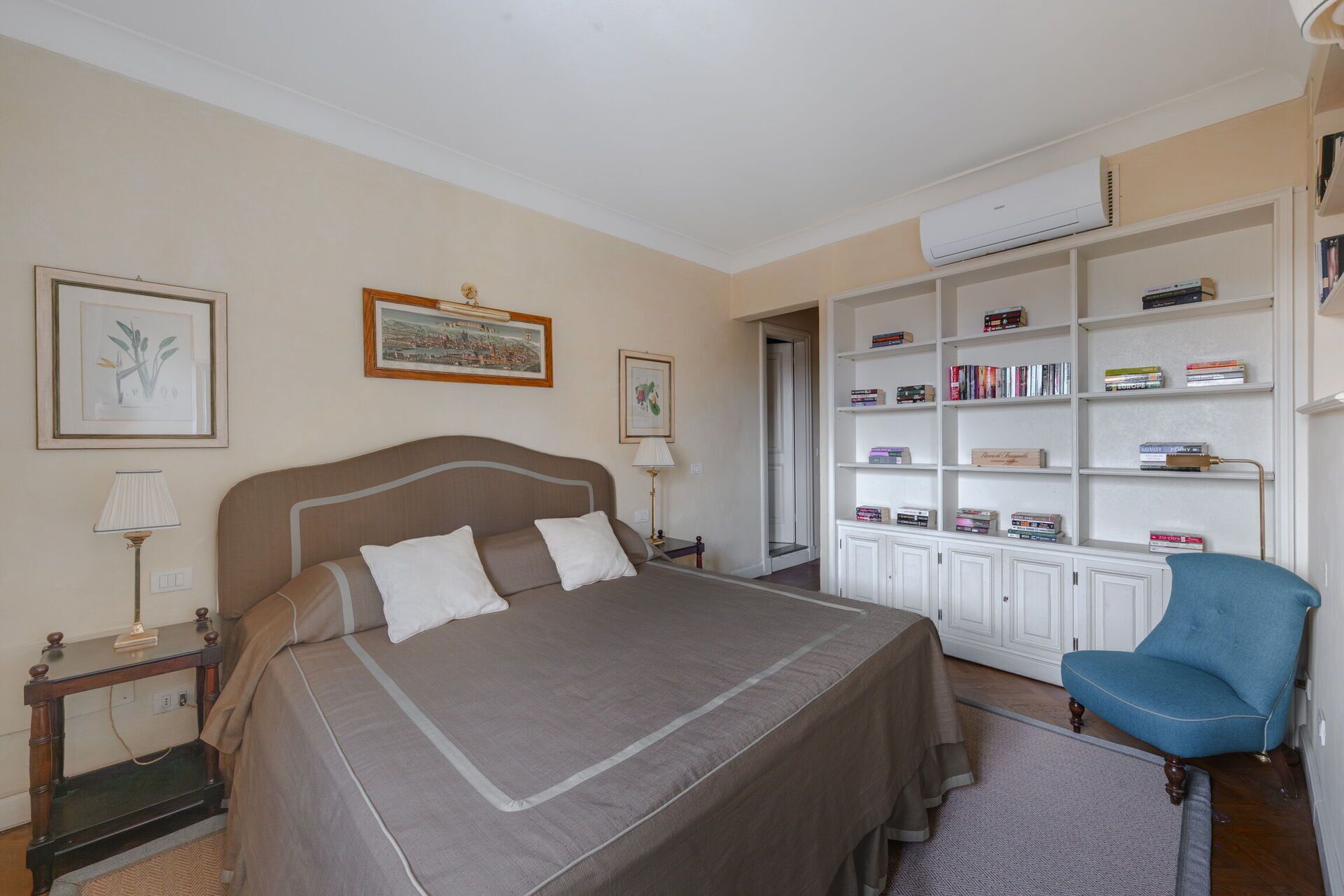 A bedroom with a large bed, a bookshelf, a desk, and a chair.