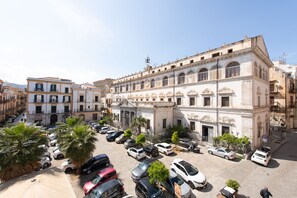 Un edificio histórico con un patio central, rodeado de coches aparcados y palmeras.